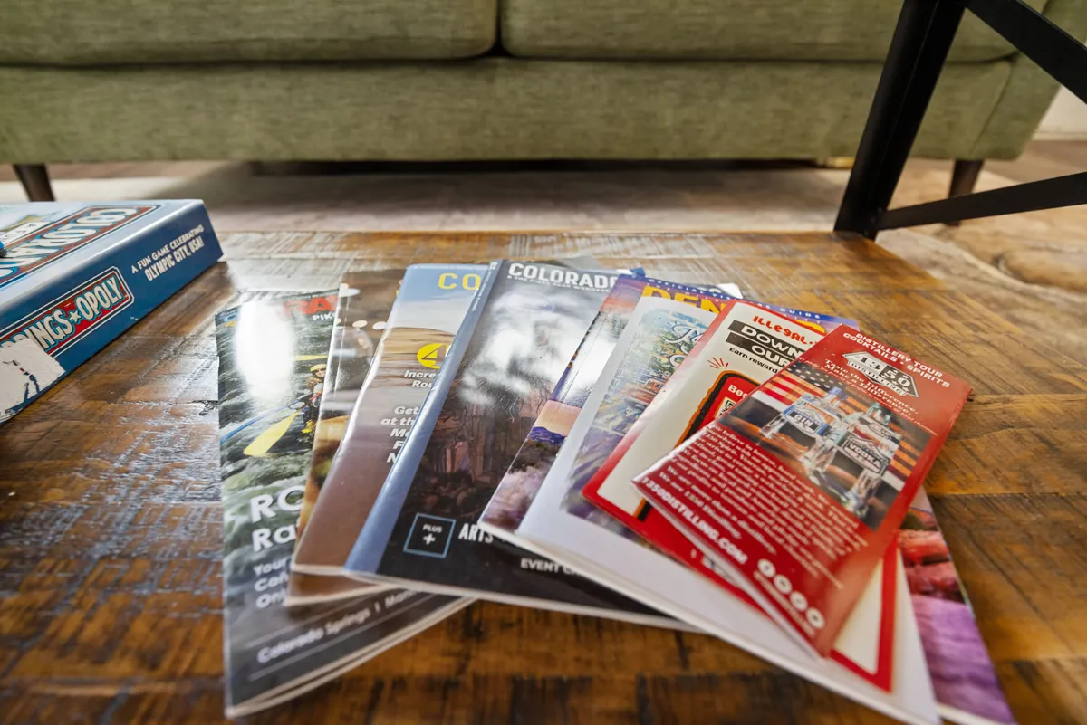 A comfortable lounge area with a green sofa, wooden coffee table displaying brochures and pamphlets, and a board game. The setup encourages relaxation, planning outings, and enjoying downtime with friends or colleagues.