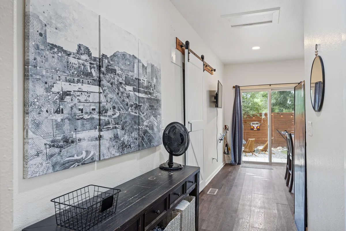 A welcoming interior living space with large wall art, a sliding barn door, ceiling fan, and an open doorway leading directly to the backyard. The flow between indoors and outdoors is emphasized, inviting residents to easily transition from work to leisure activities.