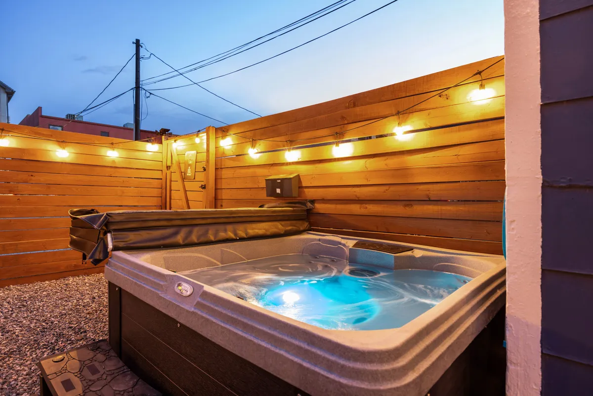 The hero image showcases a tranquil backyard oasis at dusk, with a steaming hot tub set beneath twinkling string lights, all enclosed by a warm wooden fence. The inviting setup is perfect for relaxation or casual social gatherings, evoking a sense of cozy seclusion and evening ambiance.
