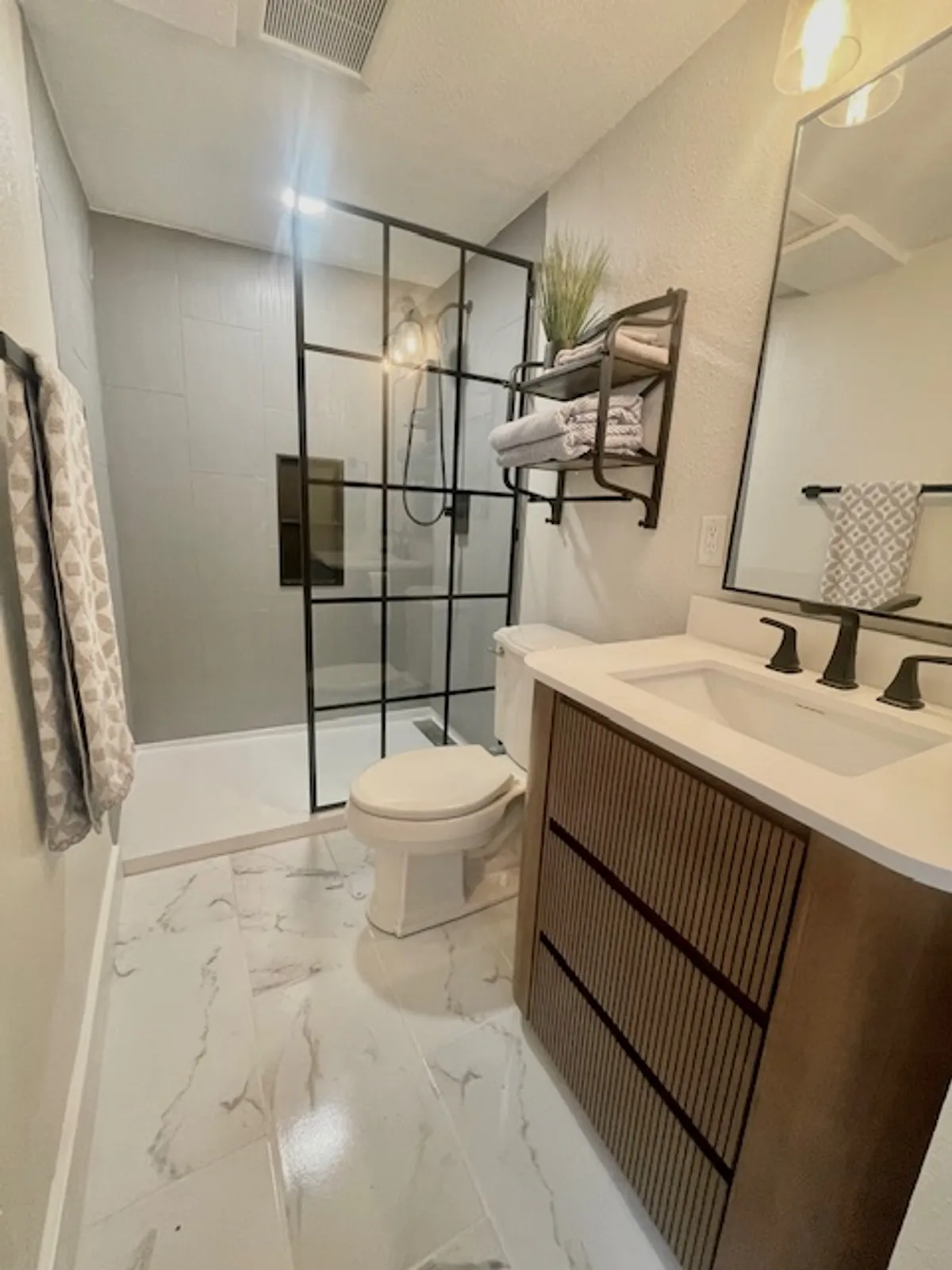 A modern bathroom with a glass shower enclosure, stylish vanity and sink, and neatly arranged towels on decorative shelving. The space feels organized, serene, and inviting—ideal for personal grooming and relaxation.